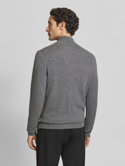 Männermodel trägt Strickjacke aus Wolle Kaschmir mit Stehkragen von BOSS in Grau, Feinstrick, gerippte Abschlüsse, Ganzkörperansicht Rückansicht.