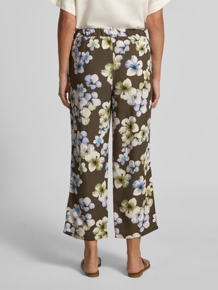 Frauenmodel trägt Hose aus Viskose-Leinen-Mix Modell 'Alexandria' von STEHMANN mit floralem Allover-Look in Braun, Ganzkörperansicht Rückansicht. Damen Hose, verkürzte Passform, Bundweite 38 cm, Innenbeinlänge 68 cm.