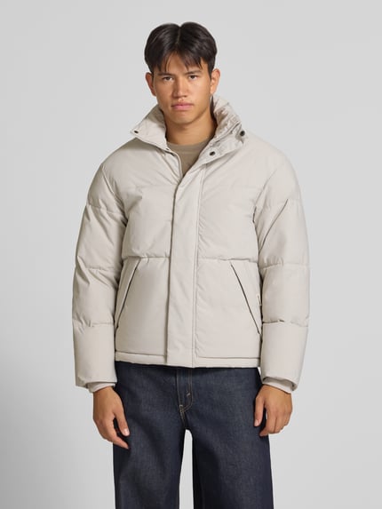 Männermodel trägt lichtbeige gewatteerd jack met opstaande kraag en ritssluiting, Model 'SOHO' van JACK & JONES, regular fit, Ganzkörperansicht von vorne. Ruglengte bij maat M 70 cm, schouderbreedte 47 cm, borstwijdte 60 cm, mouwlengte 68 cm.