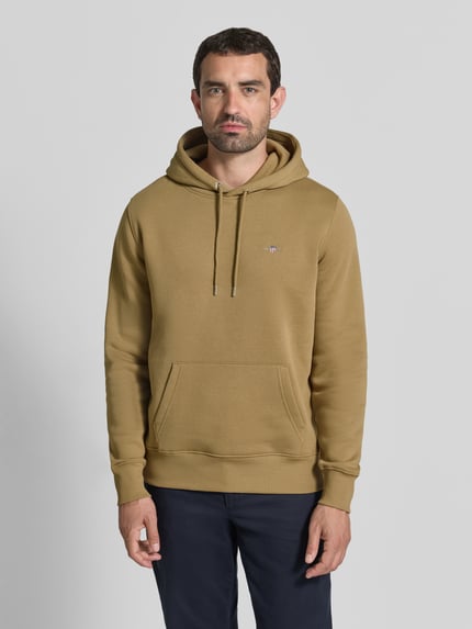 Männermodel trägt Regular Fit Hoodie aus Baumwoll-Mix von GANT in Beige mit Kängurutasche, glatte Oberfläche, Ganzkörperansicht von vorne.