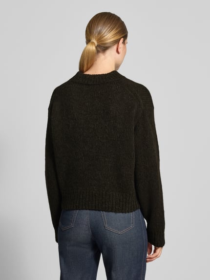 Frauenmodel trägt Relaxed Fit Strickpullover aus Woll-Alpaka-Mix von Marc Cain in Dunkelgrün, grobe Textur, Ganzkörperansicht Rückansicht. Damen Pullover, Lanawoll-Mix mit Alpaka-Anteil, gerippte Abschlüsse, überschnittene Schultern, langärmlig, Rundhalsausschnitt, Rückenlänge bei Größe 36: 51 cm, Ärmellänge: 62 cm.