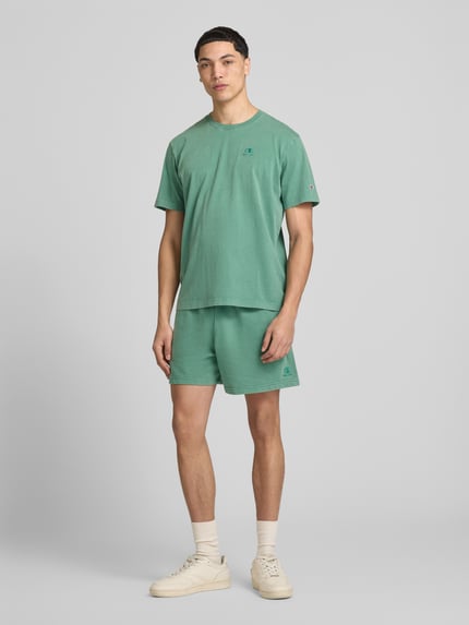 Männermodel trägt grüne Sweatshorts mit Eingrifftaschen von CHAMPION aus Baumwoll-Mix, Regular Fit, ganzkörperansicht von vorne.