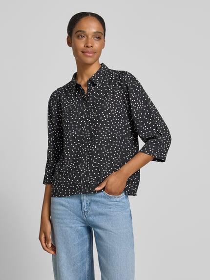 Modelka nosi bluzkę z wiskozy o kroju regular fit, model 'Bono' od LOLLYS LAUNDRY, wzór na całej powierzchni, kołnierzyk koszulowy, listwa guzikowa, rękaw o dł. 3/4, długość tyłu w rozmiarze S: 60 cm, długość rękawów: 45 cm, czarny z białymi kropkami, gładka faktura, widok całej sylwetki z przodu.