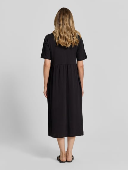 Frauenmodel trägt schwarzes Damen Midikleid mit Smok-Details Modell 'DERBY' von Soyaconcept aus reiner Baumwolle, A-Linie, Rundhalsausschnitt, Rückenlänge 117 cm, Brustweite 44 cm, Ärmellänge 27 cm, Ganzkörperansicht Rückansicht.