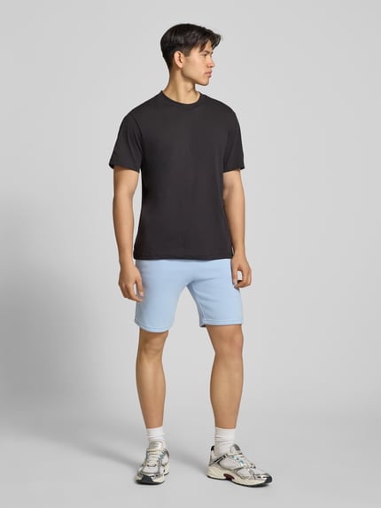 Männermodel trägt Shorts mit Eingrifftaschen und Logo-Print von Alpha Industries aus Baumwoll-Mix, Relaxed-Fit, hellblau, Ganzkörperansicht von vorne.
