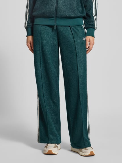Vrouwenmodel draagt Sweatpants mit elastischem Bund van adidas Originals, los vallend, glittereffect, ritszakken, Nahaufnahme onderlichaam.