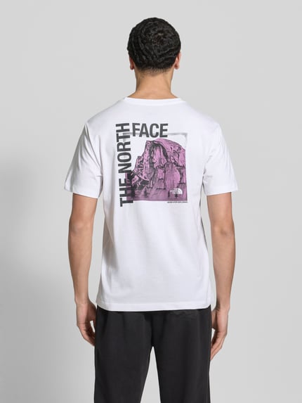 Männermodel trägt T-Shirt mit Logo und Rundhalsausschnitt von The North Face, wit met zwart en paars, regular fit, katoenmix, Ganzkörperansicht Rückansicht.