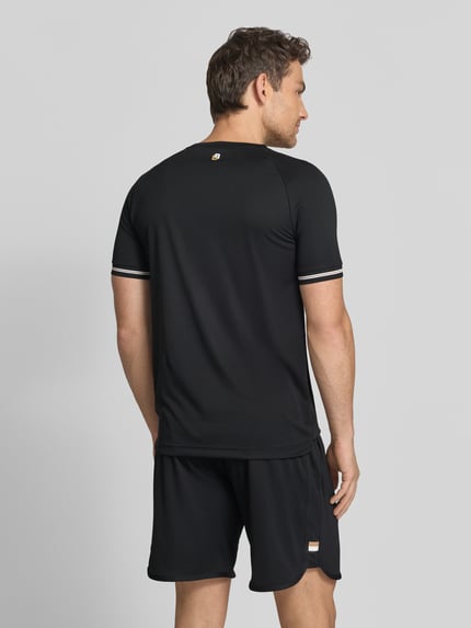 Männermodel trägt Regular Fit T-Shirt mit Label Print Modell 'TOC SERVE 2' von BOSS Green in Schwarz, Kontraststreifen, elastisch, Ganzkörperansicht Rückansicht.