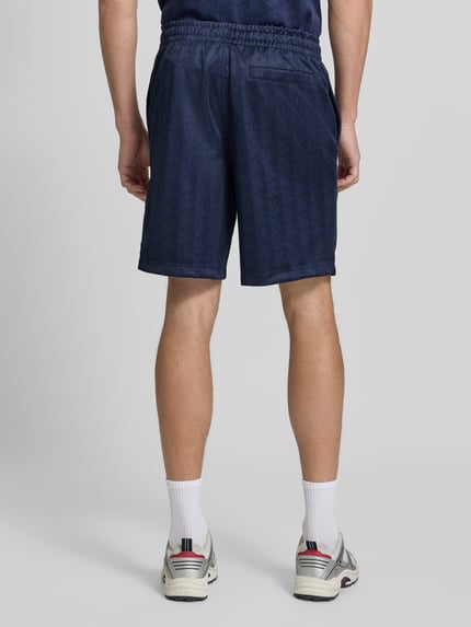 Männermodel trägt Regular Fit Sweatshorts mit Tunnelzug von Lacoste in Dunkelblau mit dezentem Muster, Ganzkörperansicht Rückansicht. Herren Sweatshorts von Lacoste.