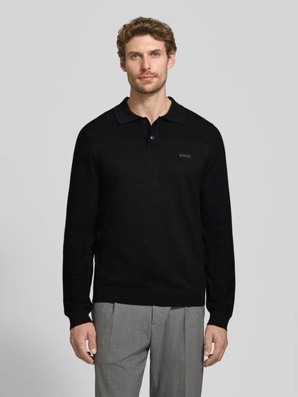 Mężczyzna nosi czarną koszulkę polo z dodatkiem wełny Relaxed Fit Poloshirt mit Woll-Anteil Modell 'KN_Momentum-X PL' od BOSS Green, szare spodnie, gładka struktura, Ganzkörperansicht von vorne.