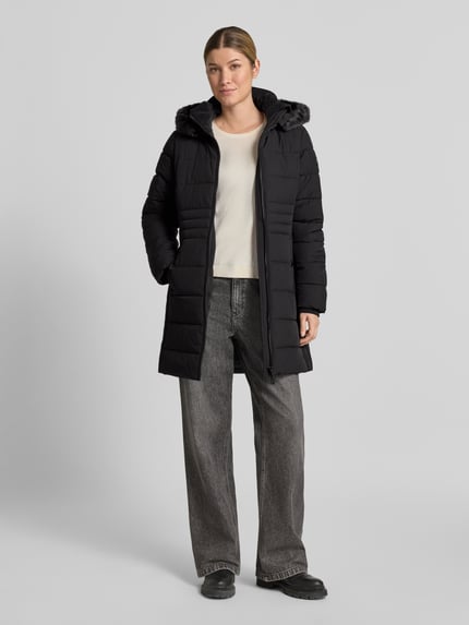 Frauenmodel trägt schwarze Jacke mit abnehmbarer Kapuze Modell 'ECLIPSE' von NAUTGÅRD, Zweiwege-Reißverschluss, Ganzkörperansicht von vorne.