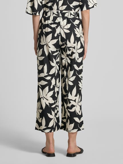 Vrouwenmodel draagt Wide Leg Culotte uit viscosemix van s.Oliver RED LABEL met all-over motief, elastische boord, zij-steekzakken, crêpe materiaalverwerking. Ganzebody aanzicht achteraan.