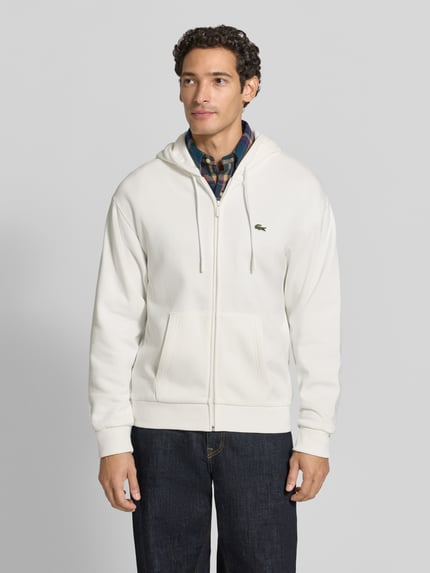 Męski model nosi Regular Fit Sweatjacke aus Baumwoll-Mix od Lacoste, bluza rozpinana w kolorze ecru, gładka faktura, Ganzkörperansicht von vorne.