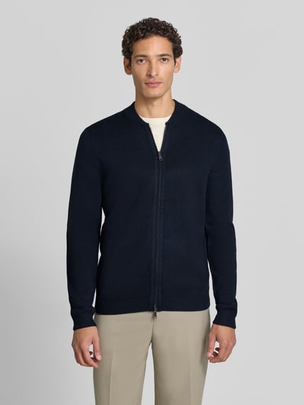 Männermodel trägt Slim Fit Strickjacke aus Baumwoll-Mix mit Stehkragen von Christian Berg Men in Dunkelblau, Zweiwege-Reißverschluss, gerippte Abschlüsse, Ganzkörperansicht von vorne.