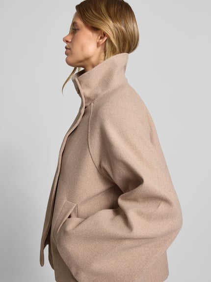 Frauenmodel trägt Jacke mit Stehkragen und Kimonoärmeln von Gina Tricot in Beige mit geradem Schnitt und Knopfleiste, Seitenansicht, Nahaufnahme Oberkörper. Rückenlänge 50 cm, Schulterbreite 44 cm, Brustweite 56 cm, Ärmellänge 60 cm.