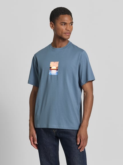 Männermodel trägt Regular Fit T-Shirt aus reiner Baumwolle Modell 'ASPEN' von SELECTED HOMME in Optik: Unifarben mit Motiv-Print, Rundhals, Kurzarm, Materialverarbeitung: Jersey, Ganzkörperansicht von vorne.