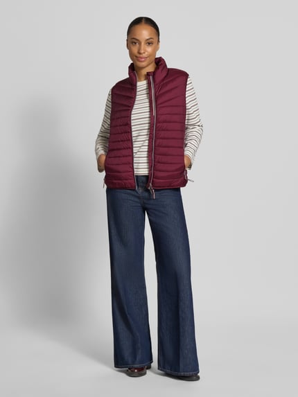 Vrouwenmodel draagt bodywarmer in stiksels van FUCHS SCHMITT, bordeaux, getailleerd, opstaande kraag, tweewegritssluiting, ruglengte maat 36: 55 cm, schouderbreedte maat 36: 39 cm, borstwijdte maat 36: 48 cm; volledige vooraanzicht