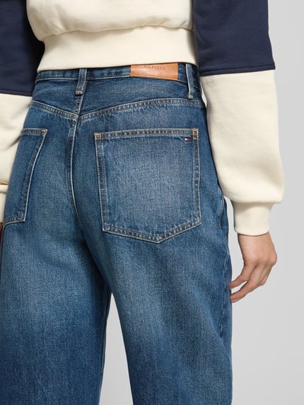 Frauenmodel trägt Tapered Fit Jeans aus reiner Baumwolle von Tommy Hilfiger in blauer Denim-Optik mit Label-Patch, Nieten und 5-Pocket-Design, Ganzkörperansicht Rückansicht