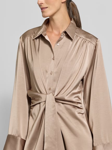 Frauenmodel trägt knielanges Hemdblusenkleid mit Knotendetail Modell 'Biria' von Neo Noir in Satin, gerader Schnitt, Nahaufnahme Oberkörper.