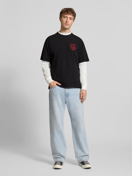 Männermodel trägt Herren T-Shirt aus Reiner Baumwolle Modell 'MUSIC CHANNEL' von Edwin, schwarze Töne, Gerader-Schnitt, Ganzkörperansicht von vorne. Rückenlänge bei Größe M: 70 cm, Rundhalsausschnitt.