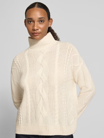 Vrouwenmodel draagt pullover van kasjmier met kabelpatroon van Christian Berg Woman, recht model, opstaande kraag, ribboorden, ruglengte maat S 57 cm, mouwlengte maat S 64 cm, crèmekleur, grof gebreide textuur, vooraanzicht bovenlichaam.