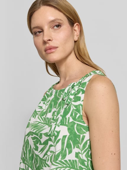 Frauenmodel trägt Blusenshirt mit Binde-Detail und Rundhalsausschnitt von More & More aus Reine Viskose, Gerade, grün-weißes Blattmuster, Nahaufnahme Oberkörper.