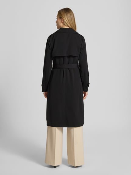 Modelka nosi czarny trencz dwurzędowy z wiązanym paskiem od MICHAEL Michael Kors, krój regular fit, widok całej sylwetki z tyłu. Długość tyłu w rozmiarze S: 47 cm, szerokość ramion w rozmiarze S: 40 cm, szerokość w klatce piersiowej w rozmiarze S: 50 cm, długość rękawów w rozmiarze S: 63 cm.