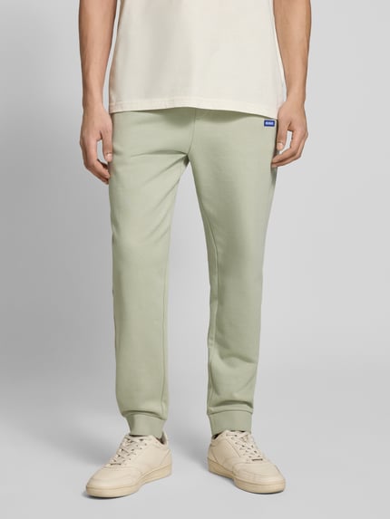 Männermodel trägt Relaxed Fit Sweatpants aus reiner Baumwolle Modell 'NAPIN`' von Hugo Blue, jednokolorowy, naszywka z logo, tunel, elastyczny ściągacz, prążkowane zakończenia nogawek, wpuszczane kieszenie, wykończenie materiału: dzianina dresowa, bawełna; Ganzkörperansicht von vorne