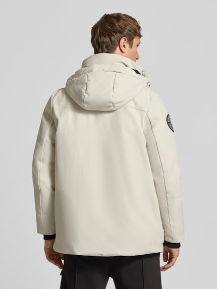 Męski model ma na sobie Parka mit Kapuze und Pattentaschen od Superdry w kolorze jasnobeżowym, krój regular fit, kaptur, kieszenie z patką, długość tyłu w rozmiarze M: 80 cm, szerokość ramion w rozmiarze M: 48 cm, szerokość w rozmiarze M: 61 cm, długość rękawów w rozmiarze M: 73 cm, widok całej sylwetki z tyłu.