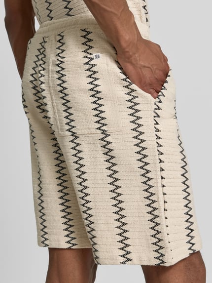 Männermodel trägt Relaxed Fit Stoffshorts aus Baumwoll-Mix von s.Oliver RED LABEL mit Strukturmuster, cremefarben mit schwarzen Linien, Nahaufnahme Rückansicht.