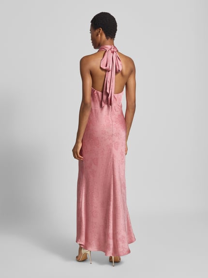 Frauenmodel trägt Abendkleid mit Neckholder Modell 'Fiona' von Neo Noir in Rosa, Satin-Stoff mit floralem Muster, Maxilänge, Ganzkörperansicht Rückansicht. Taillierte Passform, Stehkragen, Rückenlänge bei Größe 36: 139 cm, Brustweite: 38 cm.