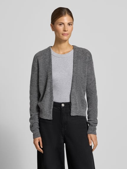 Frauenmodel trägt Regular Fit Strickjacke aus Alpaka-Mix mit Baumwoll-Anteil von DRYKORN, Modell 'LOBAIA', meliertes Grau, weiche Textur, V-Ausschnitt, dezente Strickstruktur, Ganzkörperansicht von vorne.