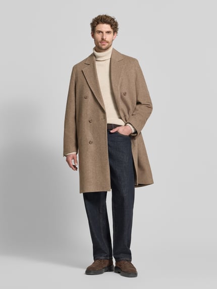 Männermodel trägt Mantel mit Reverskragen und Eingrifftaschen Modell 'NEKOLA' von DRYKORN im Baumwoll-Mix in Beige, Ganzkörperansicht von vorne.