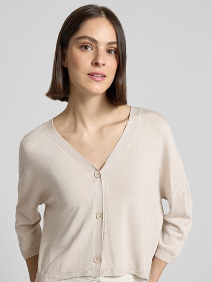 Frauenmodel trägt Schimmernde Strickjacke mit 3/4-Arm von comma in Beige, V-Ausschnitt, Knopfleiste, Relaxed Fit, Nahaufnahme Oberkörper.