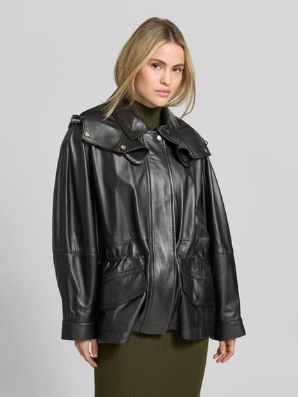 Frauenmodel trägt Funktionsjacke Modell 'GROOVE' von IRO in schwarzer Lederoptik mit metallischen Akzenten und Tunnelzug, Nahaufnahme Oberkörper.