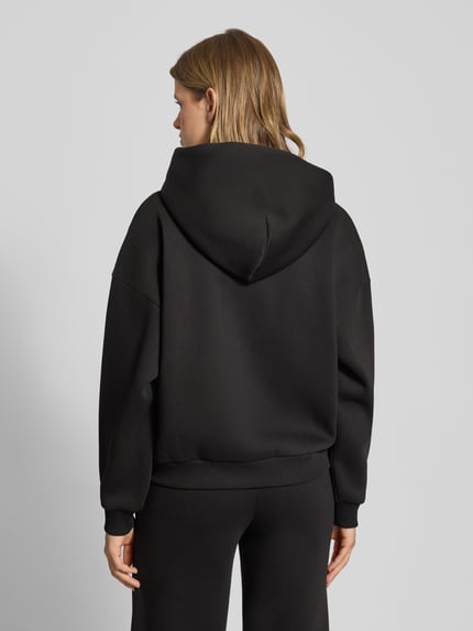 Frauenmodel trägt Hoodie mit Kapuze von Review, schwarz, Baumwoll-Mix, lockerer Schnitt, Ziersteinbesatz, Känguru-Tasche, Rippenbündchen, Ganzkörperansicht Rückansicht.