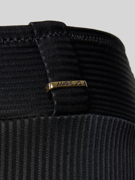 Frauenmodel trägt Bikini-Slip mit Label-Detail von Marie Jo in Schwarz, Material-Mix mit Stretch, Nahaufnahme Hüfte, elastischer Bund, strukturiertes Gewebe.