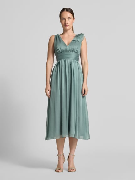 Frauenmodel trägt Cocktailkleid mit V-Ausschnitt von Swing in Grün mit Raffungen, Taillenband und Volants, Ganzkörperansicht von vorne.