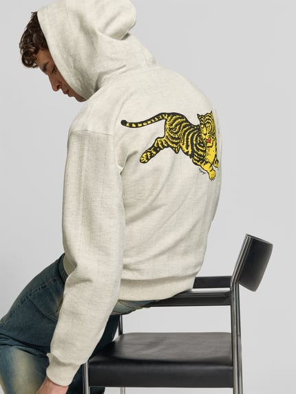 Männermodel trägt Sweatjacke mit Label-Print von Kenzo aus reiner Baumwolle, lockerer Schnitt, cremefarben mit buntem Print, Ganzkörperansicht Rückansicht. Długość pleców w rozmiarze M: 67 cm, szerokość w rozmiarze M: 55 cm, długość rękawa w rozmiarze M: 64 cm.