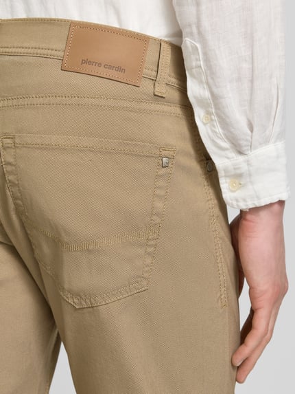 Mężczyzna nosi Fein strukturierte Hose mit Label-Detail von Pierre Cardin, beżowa, bawełniany miks ze stretchem, krój regular fit, metka, tekstura delikatna, Szerokość w rozmiarze 32/32: 43 cm, długość nogawki wewnętrznej 79 cm, detal z tyłu, zbliżenie na górną część tylnej strony