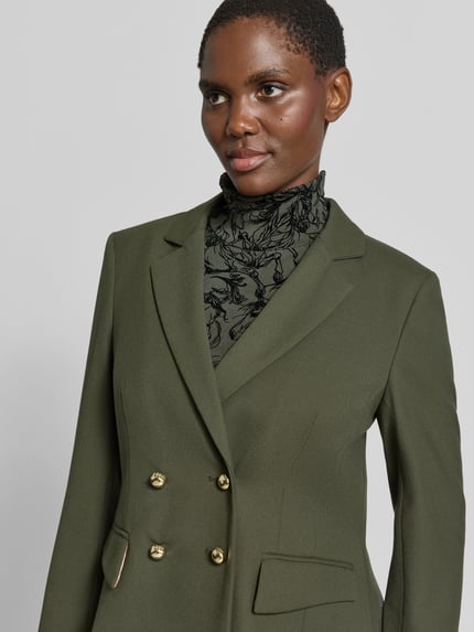 Frauenmodel trägt Slim Fit Blazer mit Reverskragen und Pattentaschen von Marc Cain im Material-Mix mit Viskose-Anteil, Nahaufnahme Oberkörper.