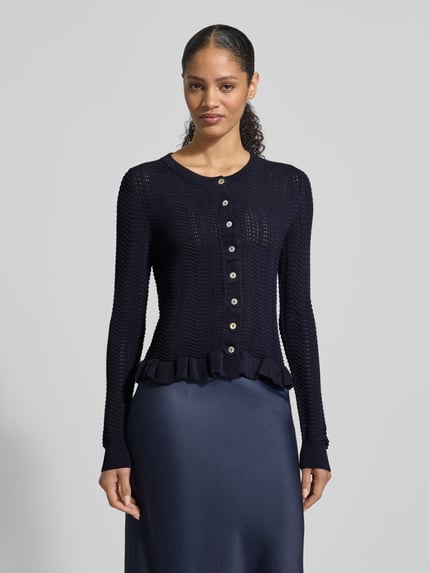 Modelka kobieca nosi Strickjacke mit Rundhalsausschnitt und Wellensaum od Christian Berg Woman Selection, krój regular fit, mieszanka materiałów z wiskozą, granatowy kolor, guziki, długość pleców w rozmiarze 36: 53 cm, długość rękawa w rozmiarze 36: 67 cm, widok całej sylwetki z przodu.