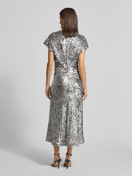 Frauenmodel trägt Maxikleid mit Pailletten- und Ziersteinbesatz von Rich & Royal, elastischer Material-Mix, taillierte Passform, Kurzärmelig, Maxilänge, Rückseite silber glänzend strukturiert, Nahtreißverschluss, Ganzkörperansicht Rückansicht.