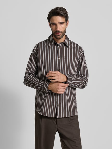 Męski model nosi Freizeithemd mit Knopfleiste Modell 'Nico' od Wood Wood, bawełna, krój luźny, brązowe paski, widok całej sylwetki z przodu.