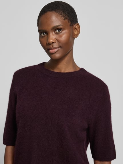 Frauenmodel trägt Relaxed Fit Strickpullover aus reiner Wolle von COMMA, dunkelviolett, weiche Textur, Halbarm, Nahaufnahme Oberkörper.