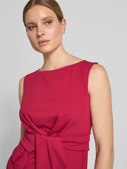 Kobiece model prezentuje Knielanges Cocktailkleid mit Knotendetail von Vera Mont, intensywny róż, materiał z domieszką stretchu, okrągły dekolt, prosty krój, detal węzła z przodu, długość do kolan, Szerokość w rozmiarze 36: 47 cm, Długość tyłu w rozmiarze 36: 93 cm, zbliżenie na górną część ciała.