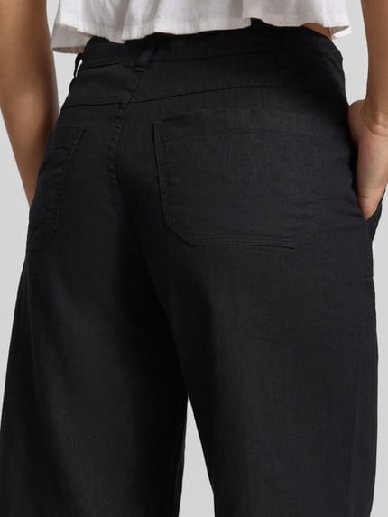 Kobiece model prezentuje Mid Waist Hose aus Leinen-Baumwoll-Mix od Gina Tricot, czarne, wpuszczane kieszenie, szerokie nogawki, tunel, mieszanka lnu i bawełny, szerokość w rozmiarze 36: 40 cm, długość wewnętrzna nogawki w rozmiarze 36: 78 cm, ujęcie detaliczne tylnej części