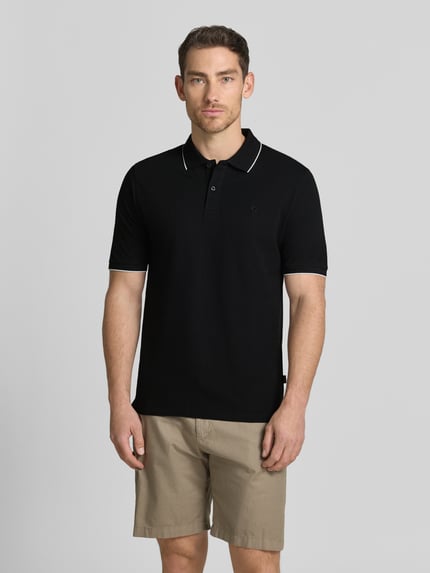 Męski model nosi Slim Fit Poloshirt mit Stitching von Jack & Jones Premium z bawełny, krój slim fit, haft, listwa guzikowa, długość tyłu w rozmiarze M: 70 cm, kolor czarny, beżowe szorty, całkowity widok z przodu.