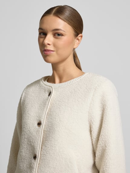 Kobiece model prezentuje Jacke mit Knopfleiste Modell 'ADA' od Vila, krój regular fit, miękki teddyfell, okrągły dekolt, zapięcie na guziki, kieszenie boczne, długość tyłu w rozmiarze 36: 57 cm, szerokość ramion w rozmiarze 36: 41 cm, szerokość w biuście w rozmiarze 36: 54 cm, długość rękawa w rozmiarze 36: 57 cm, kremowa faktura, zbliżenie na górną część ciała.
