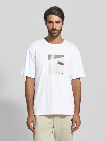 Männermodel trägt Relaxed Fit T-Shirt aus reiner Baumwolle Modell 'JOIN' von BOSS Green, weiß, Motiv-Print, Ganzkörperansicht von vorne.